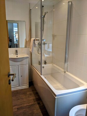 A modern bathroom with a glass-enclosed shower, a white bathtub, and a sink with a mirror above it.