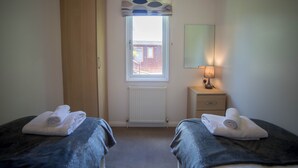 A room with two beds, a window with blinds, a radiator, a bedside table with a lamp, and a mirror on the wall. - Felmoor Park Northumberland Lodge With Hot Tub - 4 (Morpeth)