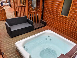 A wooden cabin with a hot tub and a wicker sofa on a wooden deck.