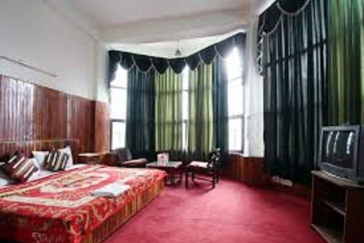Habitación de hotel con una cama grande, un escritorio, una silla, un televisor y una ventana con cortinas.