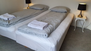 A double bed with two pillows and a folded towel, a bedside table with a lamp, and a carpeted floor. - Struer Town Apartment (Struer)