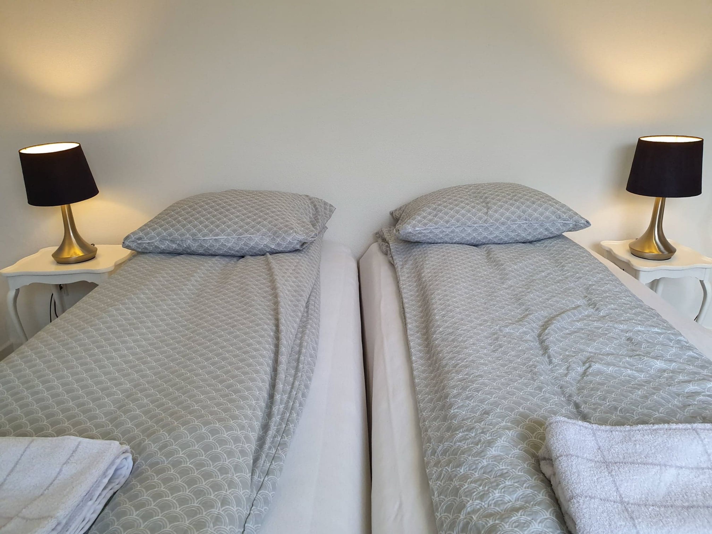 Zwei Einzelbetten mit passenden Kopfteilen, jeweils mit einer Nachttischlampe und einem Kissen mit Muster.