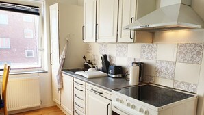 A kitchen with white cabinets, a stove, and a window with a view of a brick building. - Struer Town Apartment (Struer)