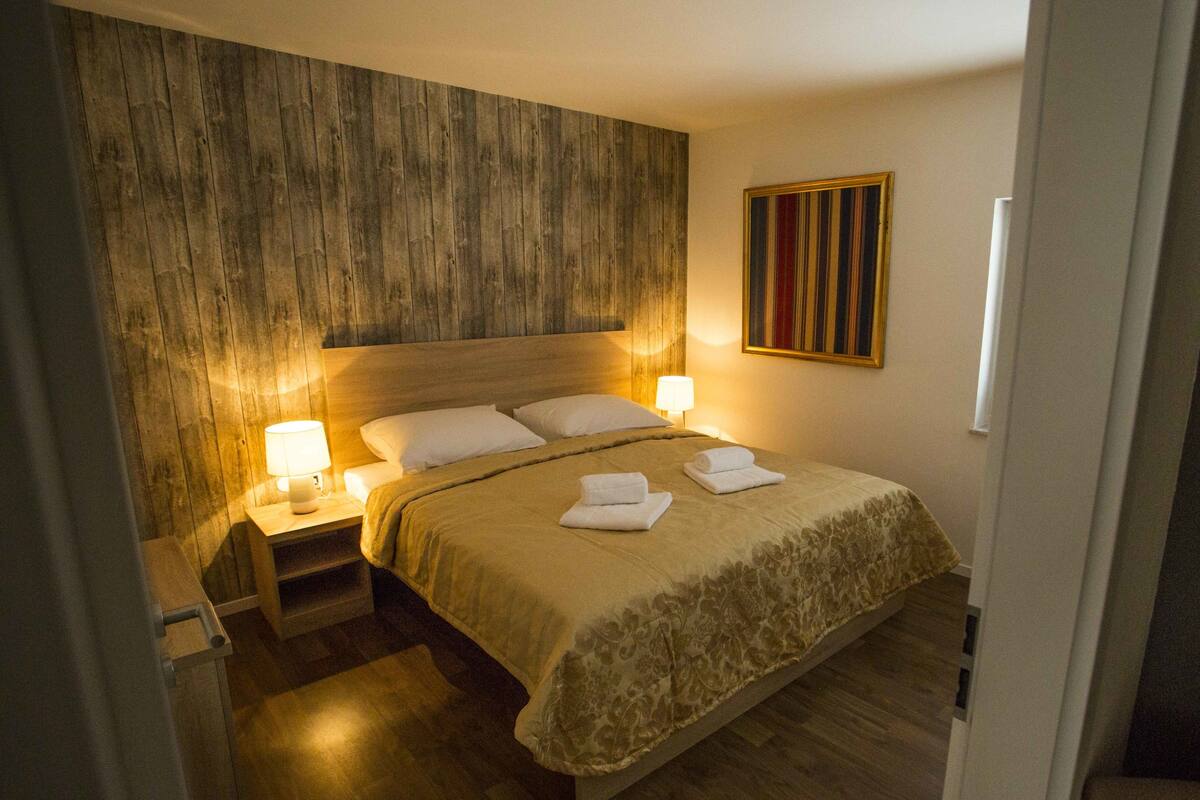 A neatly made bed with a wooden headboard, two bedside lamps, and a striped painting on the wall.