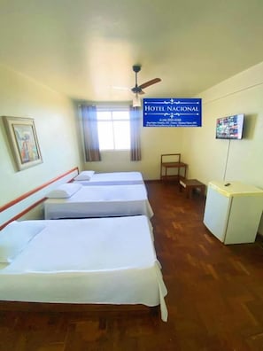 A hotel room with three beds, a desk, a television, and a ceiling fan. - Hotel Nacional Montes Claros (Montes Claros)