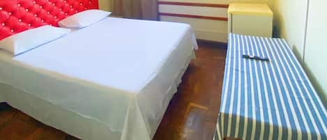 Une chambre avec un grand lit, une petite table et une tête de lit rouge recouverte de tissu.