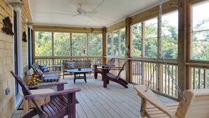 Eine Holzterrasse mit Deckenventilator, großen Fenstern und Sitzgelegenheiten, darunter Stühle und eine Bank.