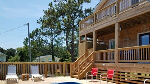 Eine Holzterrasse mit Pool, roten Stühlen und einer Treppe zu einem Balkon.