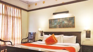 A hotel room with a large bed, a painting on the wall, and a desk with a chair. - Hotel Golden Ram Vilas (Jaipur)