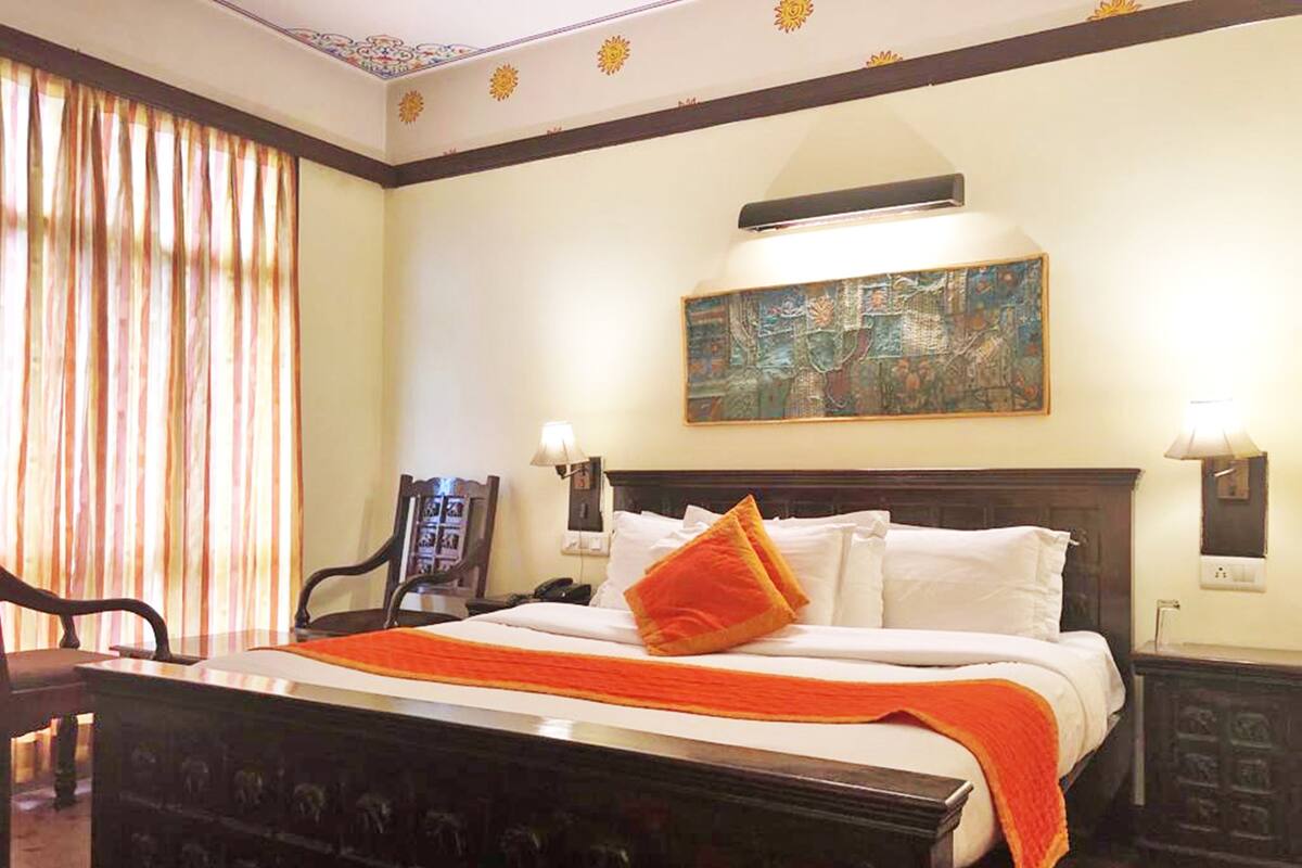 A hotel room with a large bed, a painting on the wall, and a desk with a chair.