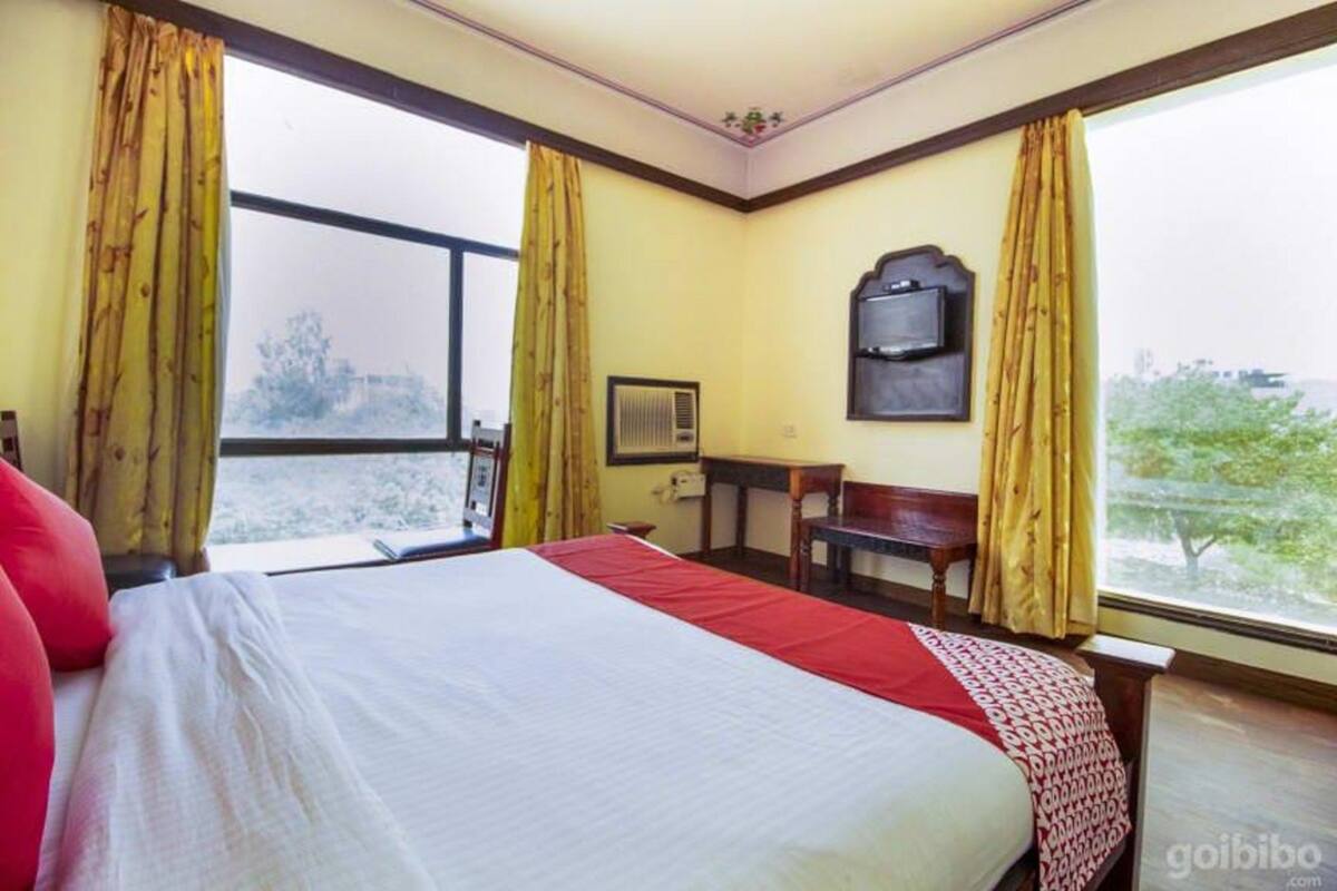 A hotel room with a bed, a desk, and a chair. There is a window with curtains, and a television on the wall.