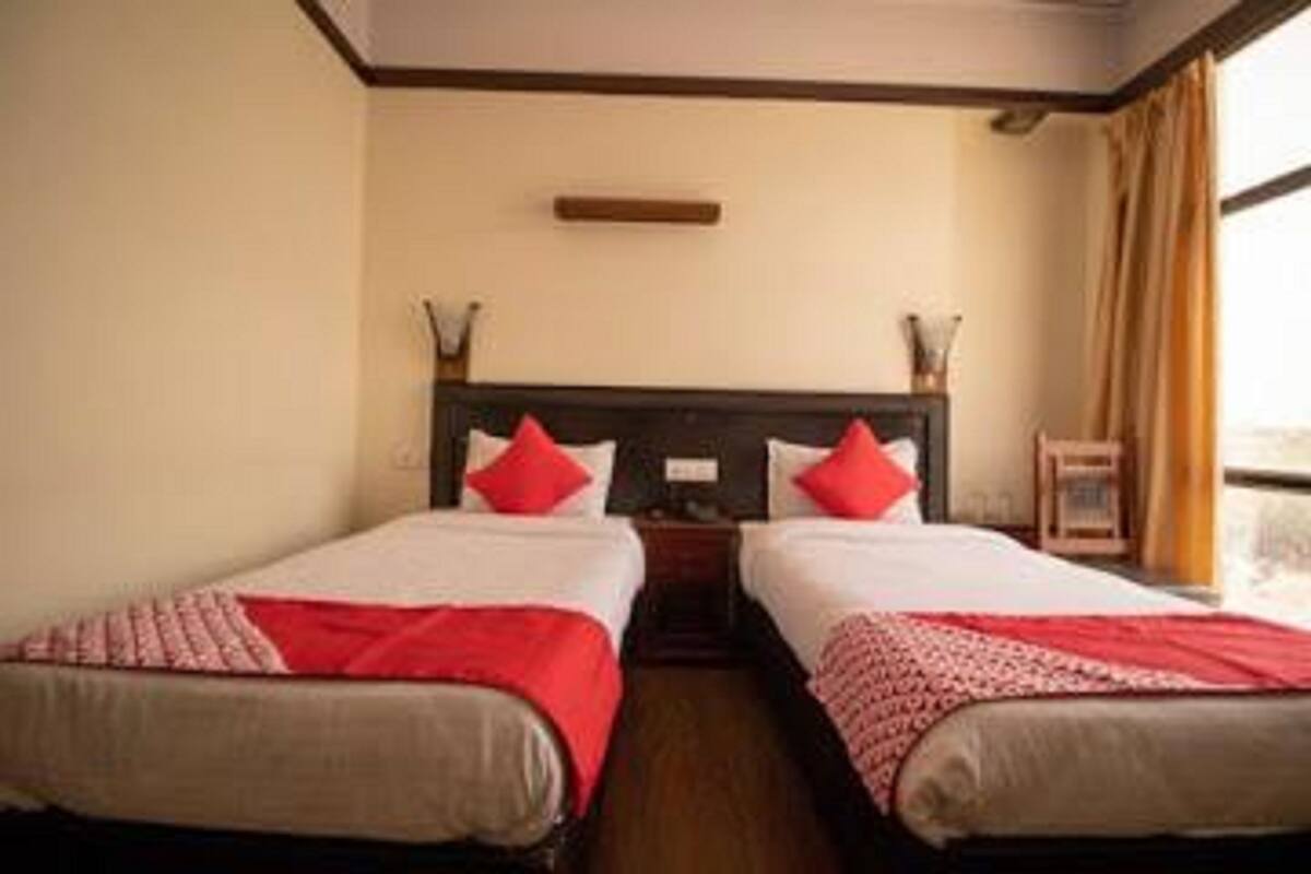 A hotel room with two single beds, each with a red and white bedspread, a wooden headboard, and a nightstand with a lamp.
