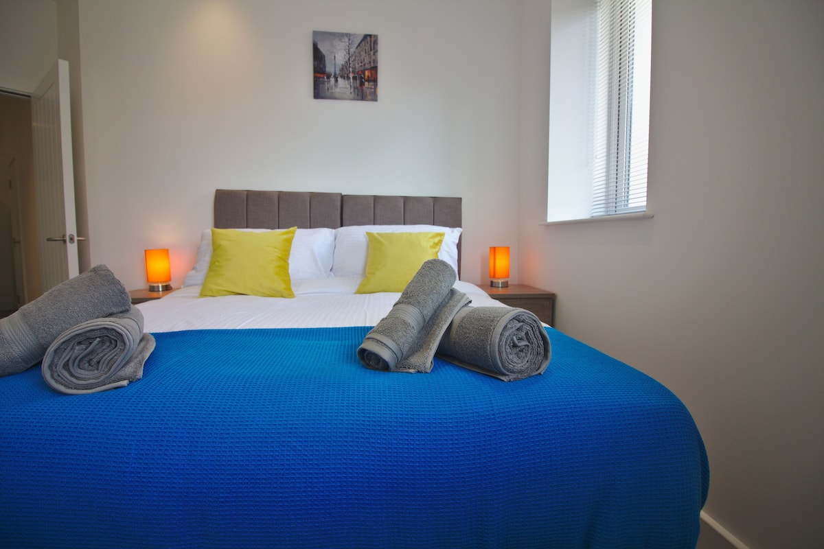 Un lit bien fait, avec une couvre-lit bleue, deux oreillers et des serviettes enroulées.