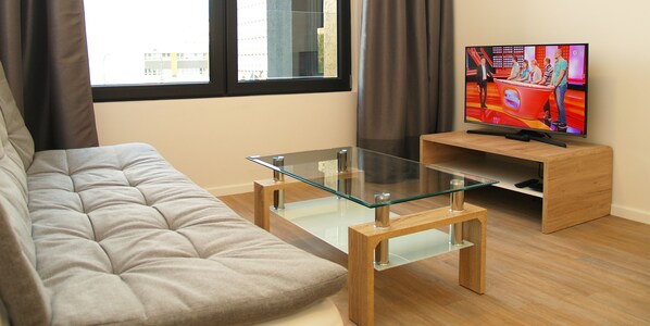 A modern living room with a sofa, a glass-top coffee table, and a wooden TV stand.