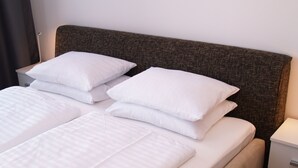 A neatly made bed with white linens and pillows, a dark textured headboard, and a bedside table with a drawer. - Quality Apartment Miletičova (Bratislava)