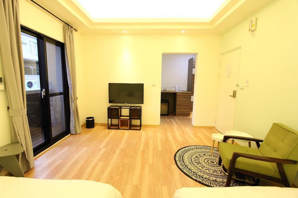 A modern living room with a flat-screen TV on a stand, a green armchair, a patterned rug, and a sliding glass door leading to a balcony.