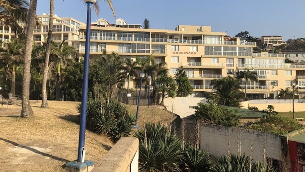 Un hotel de varios pisos con balcones, palmeras y un cielo despejado.