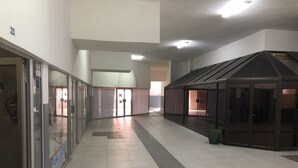 Un pasillo amplio con puertas de vidrio, un contenedor de basura y una pequeña estructura con techo inclinado.