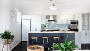 Une cuisine moderne avec des meubles blancs, un îlot central doté de tabourets, un four encastré et un four à micro-ondes.
