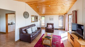 A spacious living room with a wooden ceiling, a leather sofa, a brown armchair, a wooden coffee table, and a television on a wooden stand. - Woodpecker Lodge With Hot Tub Near Cupar, Fife (Cupar)