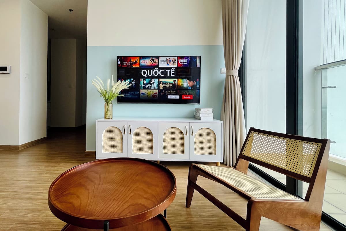 A modern living room with a flat-screen TV mounted on a white cabinet, a wooden coffee table, and a wicker sofa.