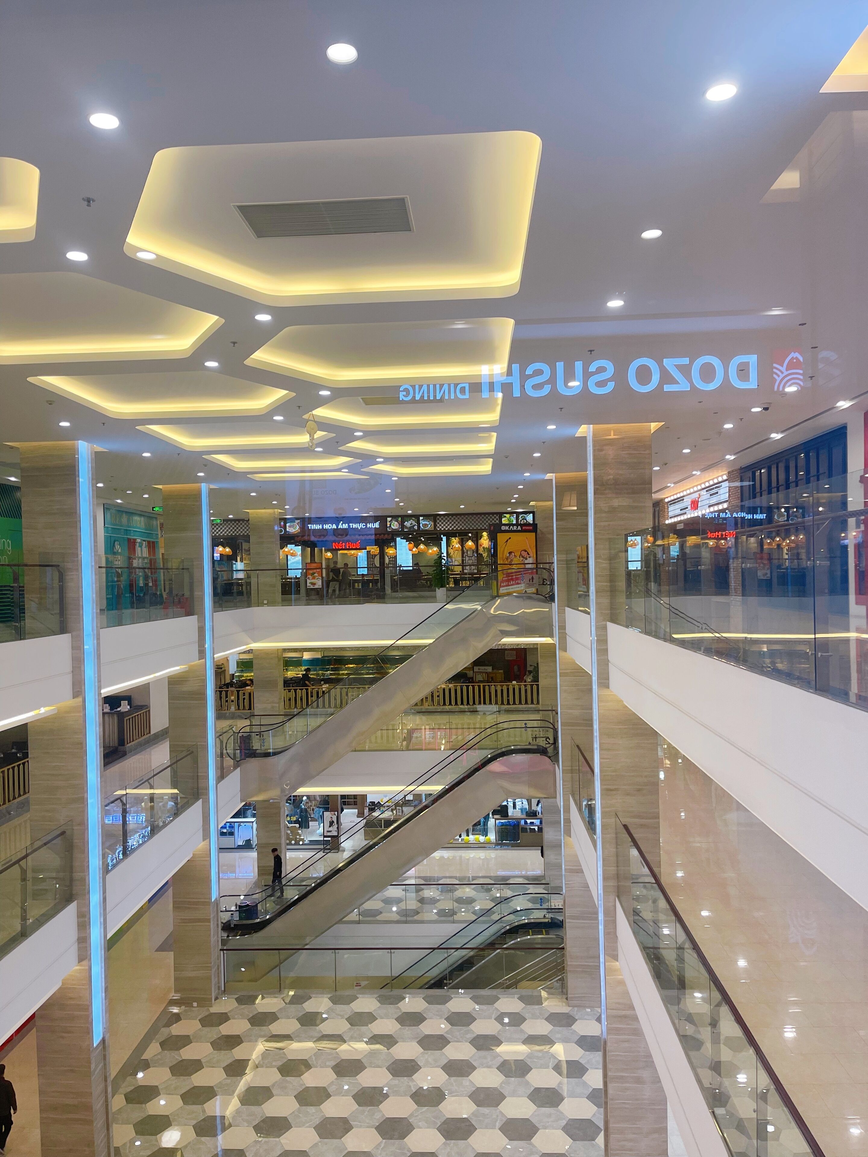Een winkelcentrum met meerdere verdiepingen, glazen balustrades, roltrappen en diverse winkels.