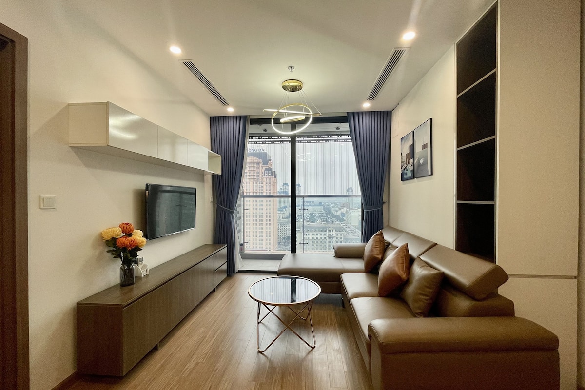 A modern living room with a sofa, a coffee table, a TV, and a view of a cityscape through large windows.