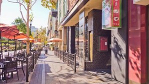 Un caffè all'aperto con tavoli e ombrelloni, un marciapiede e edifici con insegne.