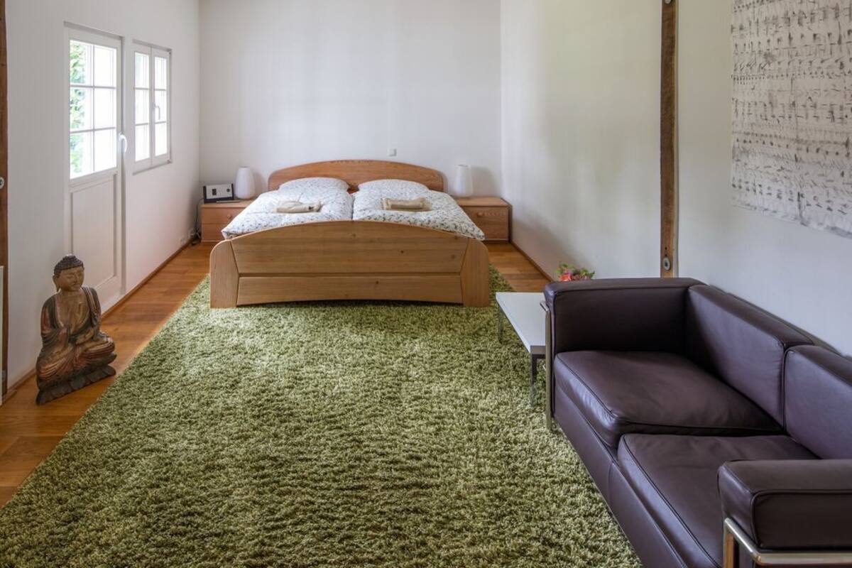 Quarto com cama de madeira, tapete verde, sofá de couro marrom e uma estátua de Buda.