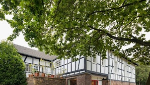 A traditional half-timbered house with a stone foundation, a red door, and a well-maintained garden. - Haus in Bewegung (Neunkirchen-Seelscheid)