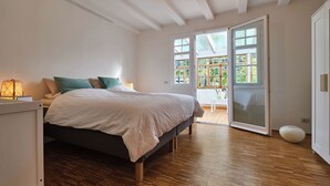 A bedroom with a bed, wooden flooring, a large window, and a door leading to a balcony. - Haus in Bewegung (Neunkirchen-Seelscheid)