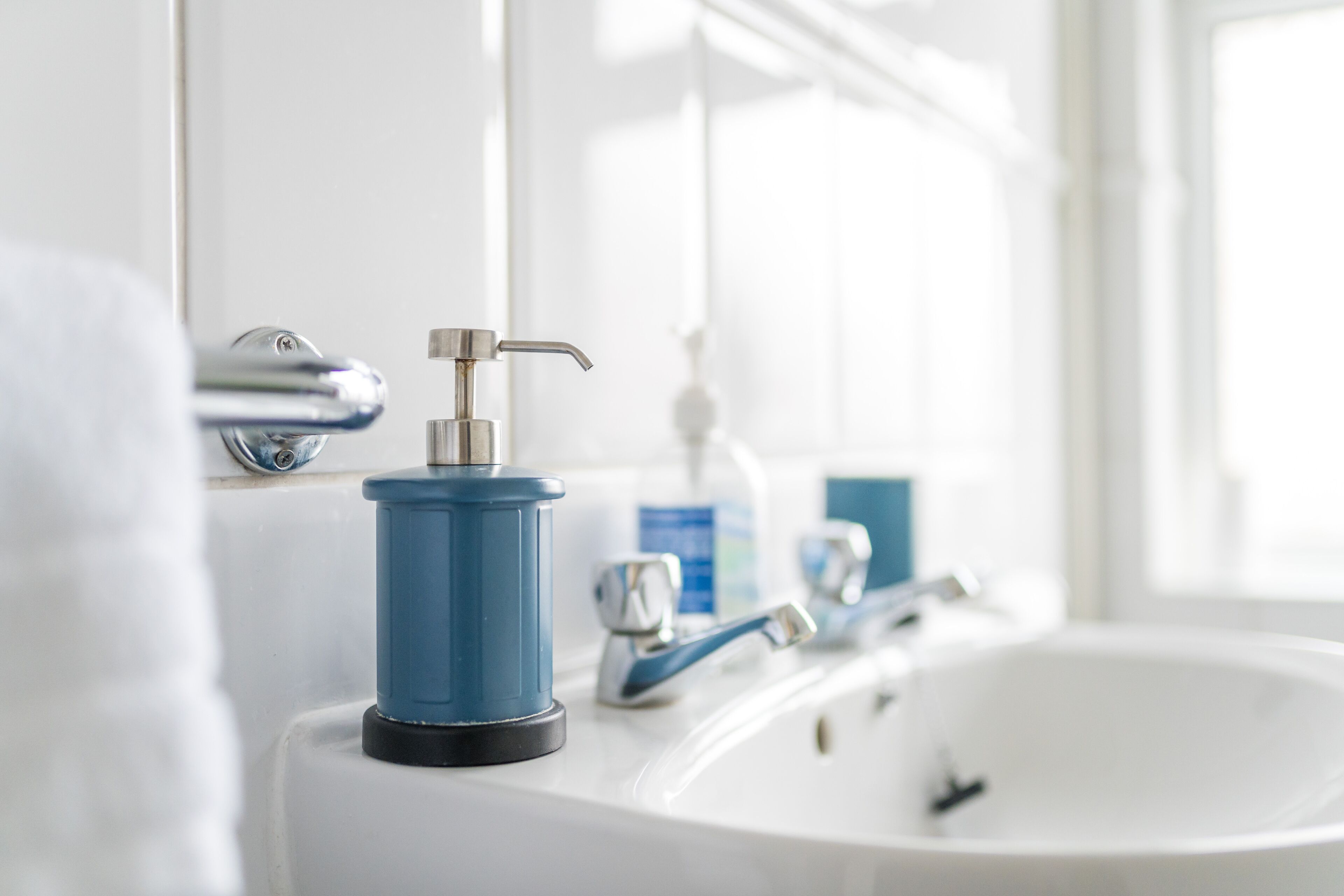 Un baño con un lavamanos blanco, un dispensador de jabón azul y un espejo.