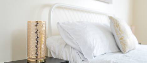 A bed with white bedding and a decorative lamp on a small black table beside it.