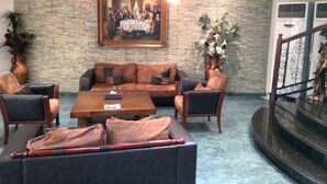 Un hall d’entrée avec un mur en pierre, un tableau représentant une scène historique, des canapés en cuir, une table basse et un escalier.