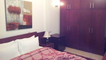 A hotel room with a bed, a nightstand, a lamp, a wardrobe, and a painting on the wall.