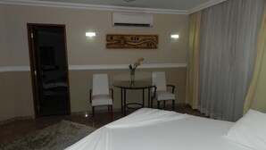 A hotel room with a bed, a desk with two chairs, a vase with flowers, and an air conditioning unit on the wall. - Paradise Inn Hotel e Lazer (Catanduva)