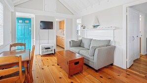 Un salón amplio con piso de madera, un sofá gris, una mesa de centro de madera y un televisor montado en la pared.