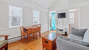 Un salón amplio con una mesa de comedor de madera, sillas, un sofá gris y un televisor montado en la pared.