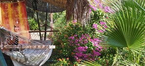 Un hamac, une structure dotée d’un toit de chaume et une variété de plantes à fleurs.