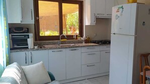 Una cocina compacta con gabinetes blancos, microondas integrado, un lavamanos y un refrigerador.