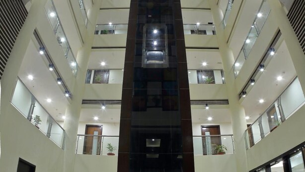 A multi-level atrium with a central elevator shaft, glass railings, and potted plants. - Incredible One Hotel (Hyderabad)