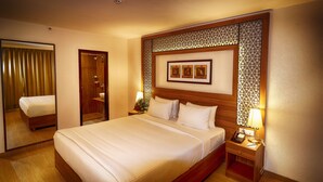 A hotel room with a large bed, a wooden headboard, a nightstand with a lamp, and a mirror. - Incredible One Hotel (Hyderabad)