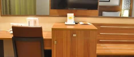 A hotel room with a wooden desk, a chair, a small cabinet, and a large mirror.