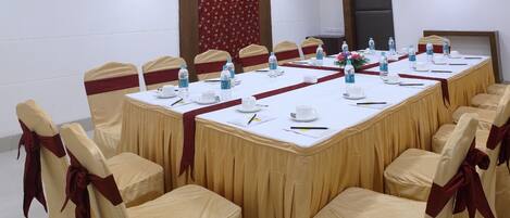 A conference room with a long table, chairs with red sashes, water bottles, and a floral arrangement.