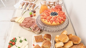 A buffet table with various food items including a fruit-topped cake, sandwiches, pastries, and a cheese platter.