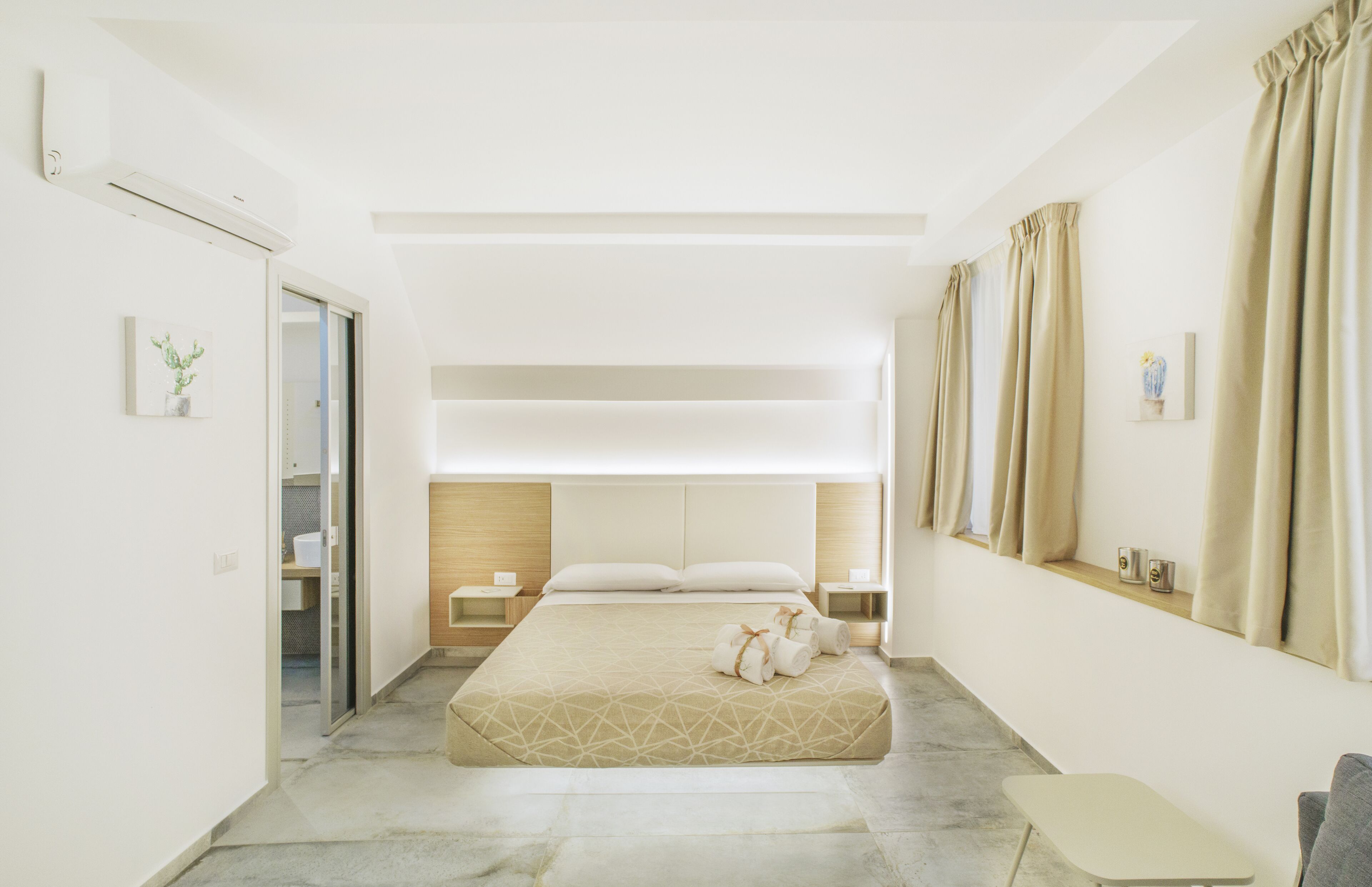 Un dormitorio moderno con una cama grande, mesitas de noche, un pequeño rincón de descanso y vistas al exterior.