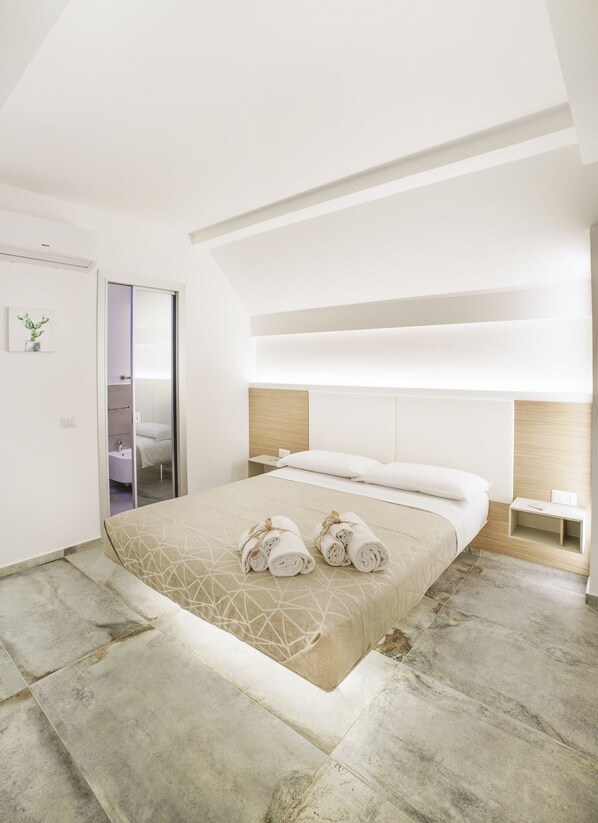 A modern bedroom with a large bed, a bedside table, a nightstand, and a bathroom visible through a door.