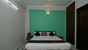 Una cama con cabecera blanca y marrón, pared verde y mesita de noche con lámpara.