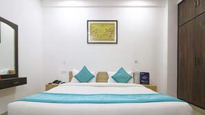 Una cama bien hecha con una manta azul, una mesita de noche con un teléfono y un libro, una obra de arte colgada en la pared y un armario de madera.