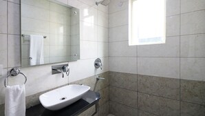 Un baño con lavamanos blanco, un espejo, un tozaleta y un cabezal de ducha.